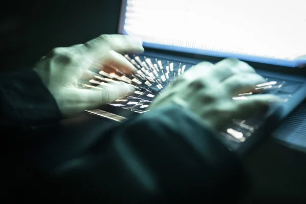 Mains tapant sur un clavier d'ordinateur portable dans une pièce sombre, illustrant l'activité en ligne.