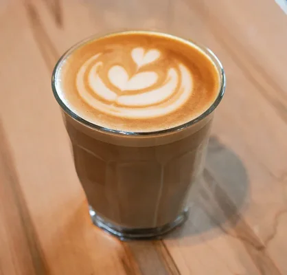 Un flat white servi dans un verre facetté, avec un cœur en latte art.