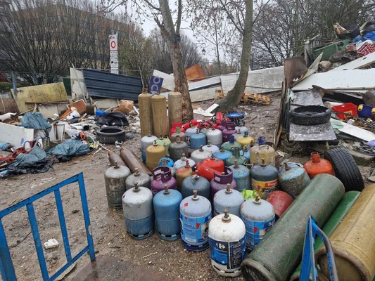 Bouteilles de propane et de gaz abandonnées dans une décharge, entourées de pneus et de débris métalliques