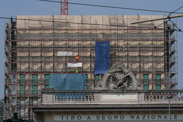 Chantier de construction du nouveau consulat américain à Milan, avec échafaudages et ouvrier au travail.
