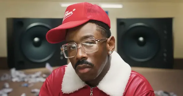 Tyler, The Creator en plan rapproché, vêtu d'une veste rouge et d'une casquette, dans un studio.