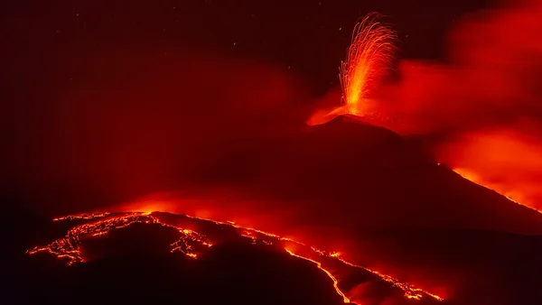 Éruption nocturne de l'Etna : fontaine de lave et coulées illuminant le ciel.