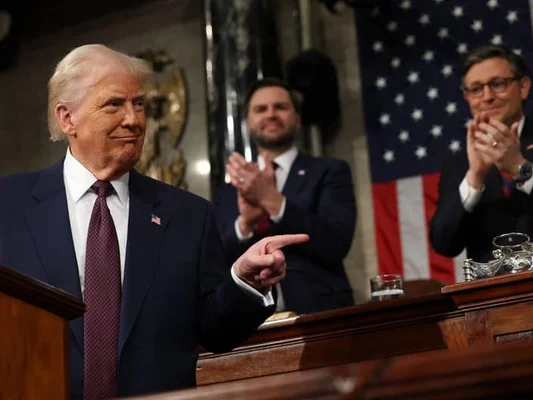 Donald Trump pointant du doigt lors d'un discours, avec des soutiens applaudissant derrière lui.