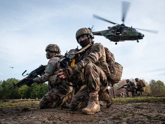 Des soldats de l'armée de Terre en exercice sur un terrain boueux, avec un hélicoptère en soutien.
