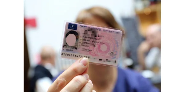 Un permis de conduire français présenté devant un visage, arrière-plan flou.