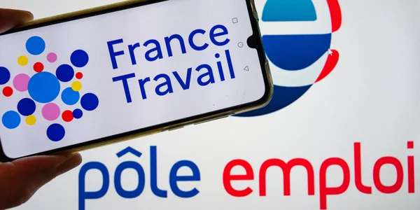 Smartphone affichant le logo de France Travail, avec l'ancien logo de Pôle emploi visible en arrière-plan.