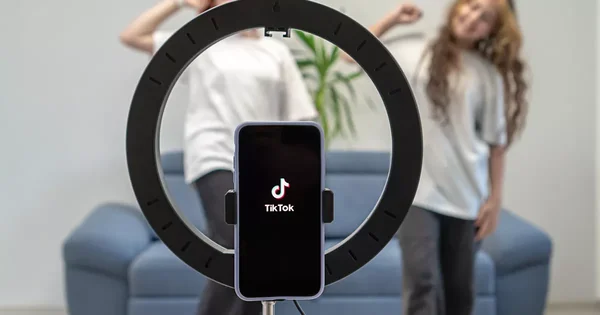 Smartphone affichant le logo de TikTok, avec une scène de danse floue en arrière-plan.