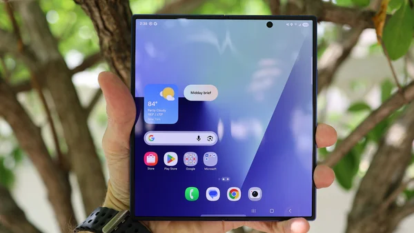 Galaxy Z Fold 8 déplié, tenu en main, avec écran d'accueil et fond d'arbres flou.