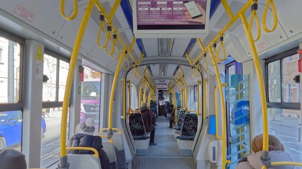 Intérieur d'un tramway moderne avec barres de maintien jaunes et passagers.