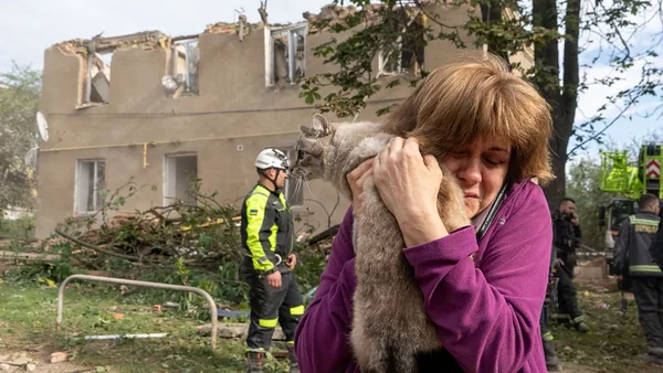 Une femme et son chat devant un immeuble détruit par une frappe, illustrant les conséquences des attaques sur les infrastructures.