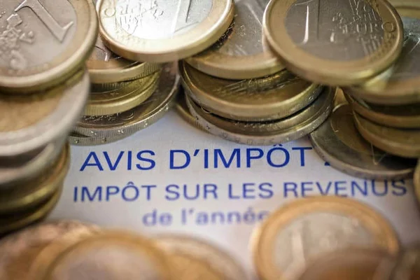 Pièces de monnaie empilées sur un avis d'impôt français, illustrant le thème fiscal.