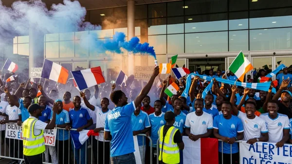 Accueil triomphal de l'OM à Abidjan : supporters en délire devant l'hôtel avec fumigène bleu et drapeaux français et ivoiriens.