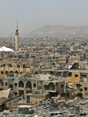 Paysage urbain dévasté par la guerre à Damas, avec un minaret de mosquée intact au second plan.