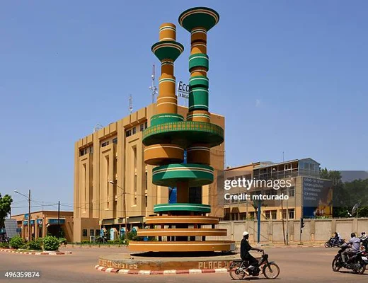 Sculpture spirale colorée sur un rond-point à Ouagadougou, devant un bâtiment officiel.