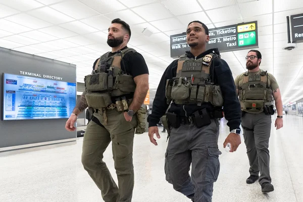 Agents de l'ICE en gilets tactiques dans un aéroport, illustrant le contexte de l'immigration et des forces de l'ordre.