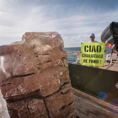 Rocher anti-chalut sur le pont du navire de Greenpeace, avec un militant tenant une pancarte de protestation.