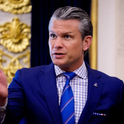 Un intervenant en costume bleu s'exprimant avec gestes dans un décor cérémoniel.