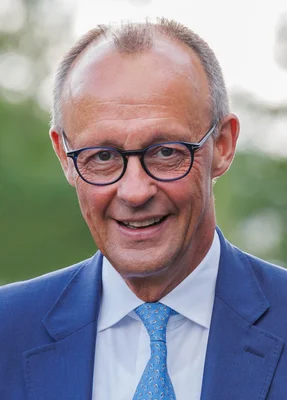 Portrait de Friedrich Merz, leader de la CDU, souriant dans un cadre extérieur.