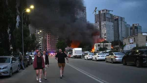Un incendie et une épaisse fumée noire dans une rue de Kiev au crépuscule, des civils s'éloignant du sinistre.
