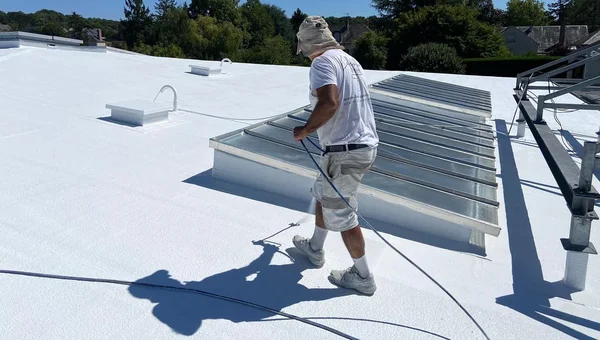 Peinture blanche appliquée sur un toit plat par un professionnel, une astuce anti-canicule gagnant en popularité.