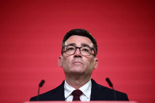 Andy Burnham au pupitre, fond rouge.