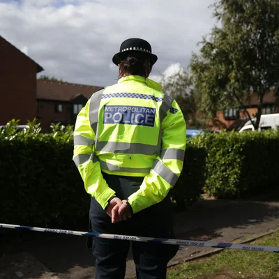 Un agent de la police métropolitaine derrière un ruban de police dans un quartier résidentiel.