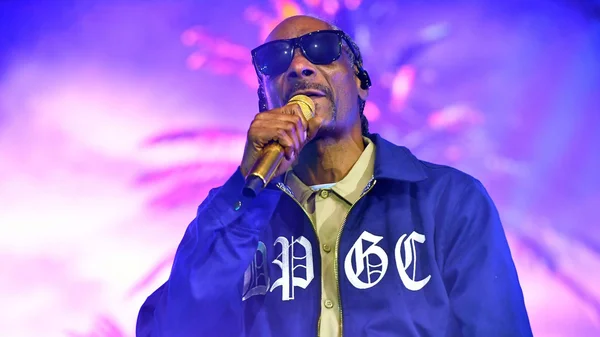 Snoop Dogg sur scène, micro doré à la main, sous un éclairage violet.