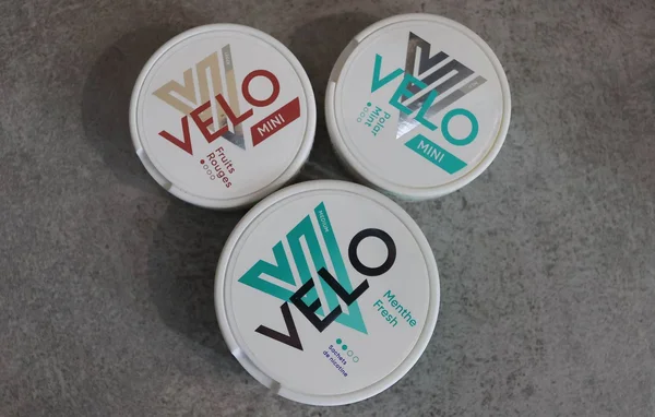 Trois boîtes de sachets de nicotine Velo Mini aux saveurs variées, disposées en triangle sur fond gris.
