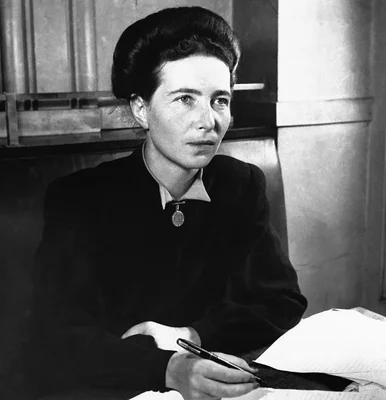 Simone de Beauvoir écrivant à son bureau, photographiée en noir et blanc.