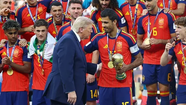 Poignée de main entre un officiel et un joueur tenant le trophée, entouré de coéquipiers médaillés.