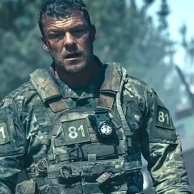 Alan Ritchson en tenue de combat dans War Machine, gilet tactique et boussole.