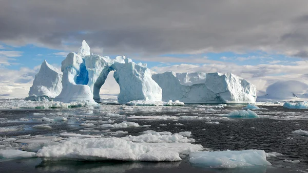 Iceberg avec une arche naturelle dans les eaux antarctiques, témoignant de la fonte des glaces.
