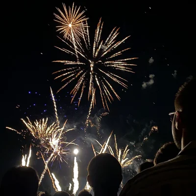 Explosions dorées d'un feu d'artifice observées par des spectateurs en contrebas.