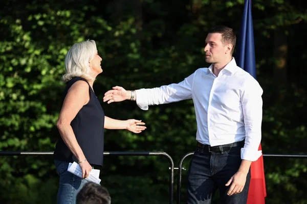 Marine Le Pen et Jordan Bardella se serrant la main en extérieur.