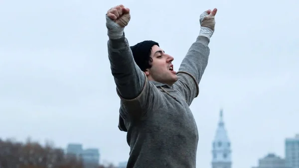 Sylvester Stallone, jeune, célèbre sa victoire devant l'hôtel de ville de Philadelphie dans le film I Play Rocky.
