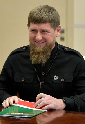 Ramzan Kadyrov souriant, assis à une table avec un dossier aux couleurs tchétchènes.