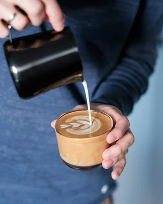 Un barista en train de verser du lait chaud pour réaliser un latte art.