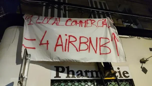 Bannière dénonçant la transformation des locaux commerciaux en logements Airbnb, devant une pharmacie à Marseille.