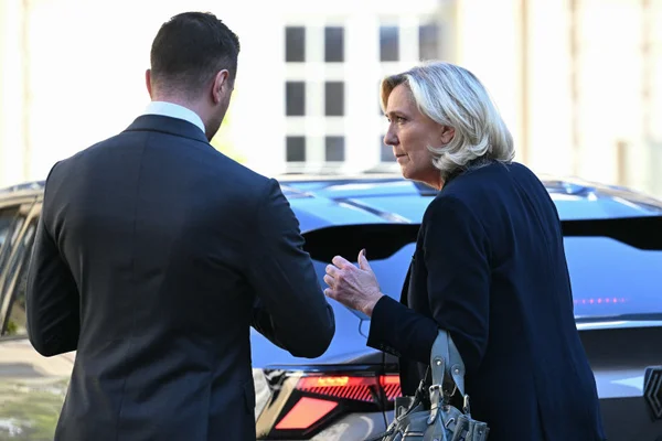 Marine Le Pen s'adressant à Jordan Bardella près d'un véhicule.