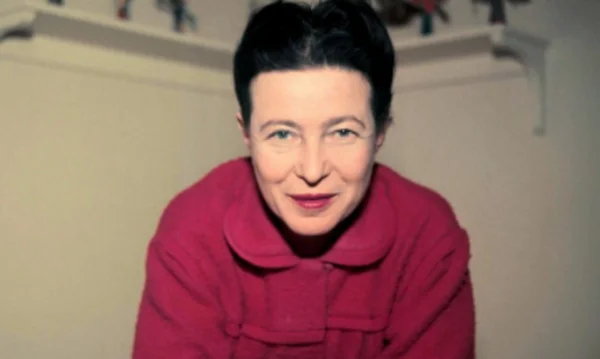 Simone de Beauvoir en manteau rouge, photographiée en plan rapproché.