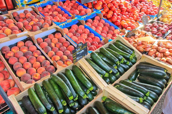 Étal de fruits et légumes sur un marché, incluant courgettes et haricots.