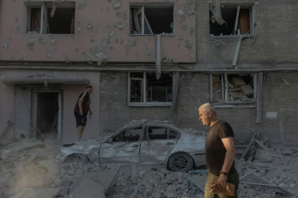 Deux hommes parmi les décombres après les frappes russes sur Kiev, avec un bâtiment endommagé et une voiture détruite.