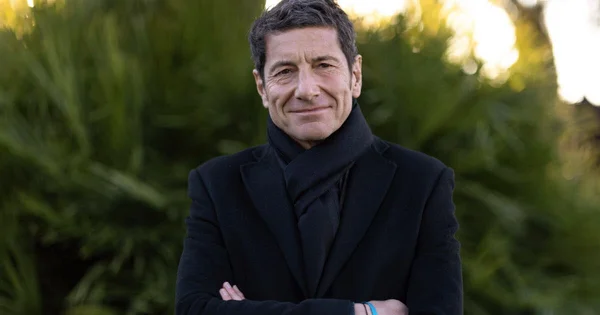 David Lisnard en manteau et écharpe, les bras croisés, souriant à l'extérieur.