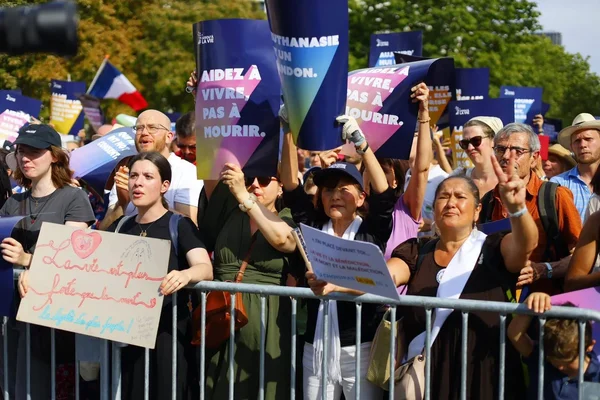 Manifestation à Paris contre la loi sur la fin de vie : des milliers de personnes derrière des barrières avec des pancartes 'Aidez à vivre, pas à mourir'.