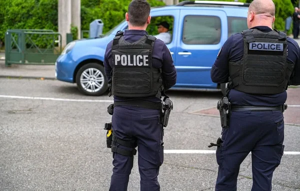 Deux agents des forces de l'ordre en tenue d'intervention, de dos, devant un fourgon de police.
