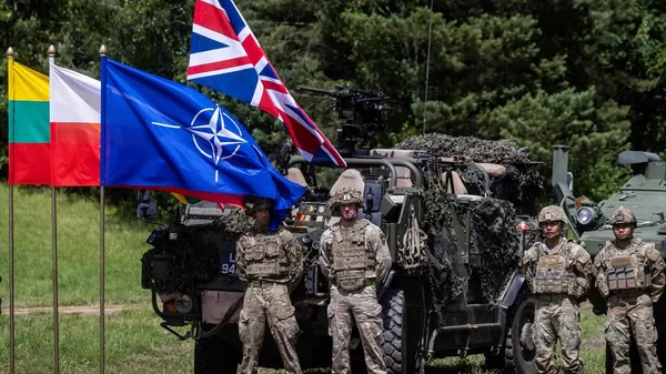 Soldats de l'OTAN devant un véhicule blindé, drapeaux de la Lituanie, Pologne, OTAN et Islande.