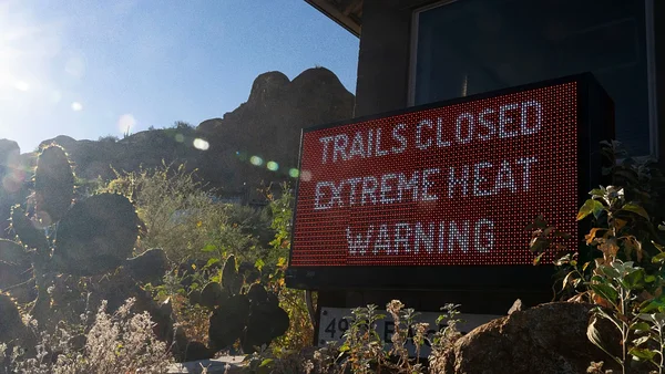 Panneau d'avertissement 'TRAILS CLOSED EXTREME HEAT WARNING' dans un paysage désertique américain.
