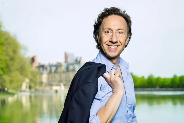 Stéphane Bern en extérieur, près d'un plan d'eau.