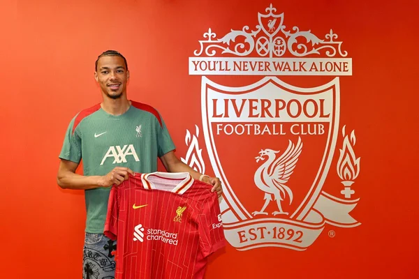 Présentation d'un maillot du Liverpool FC devant l'écusson du club.