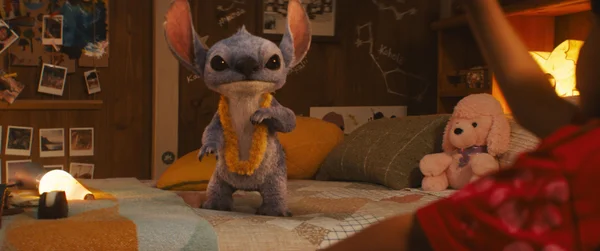 Stitch avec un lei jaune sur un lit dans une scène du film Lilo & Stitch (2025).
